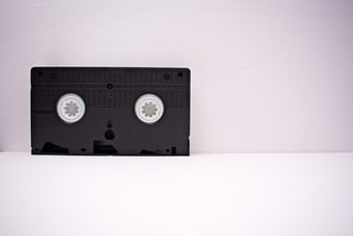 Bottom of VHS cassette tape; black with white circles; background is a light pink wall