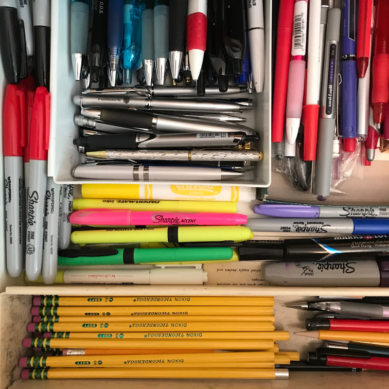 Top view of open desk drawer filled with small containers with sharpies, pens, pencils, and highlighters, some facing up and down and others facing side to side