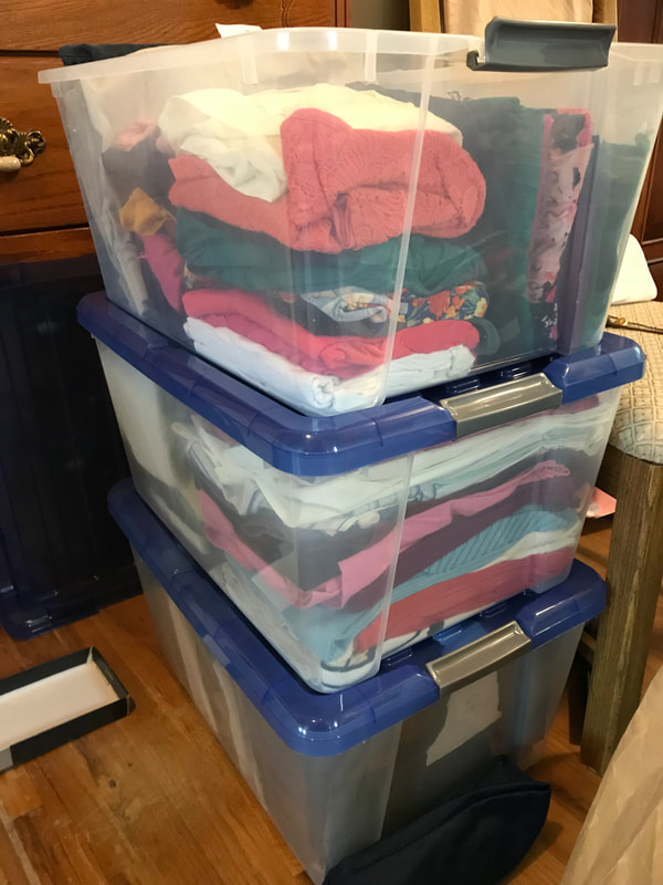 Three large clear plastic bins are shown stacked vertically with clothes folded inside.  