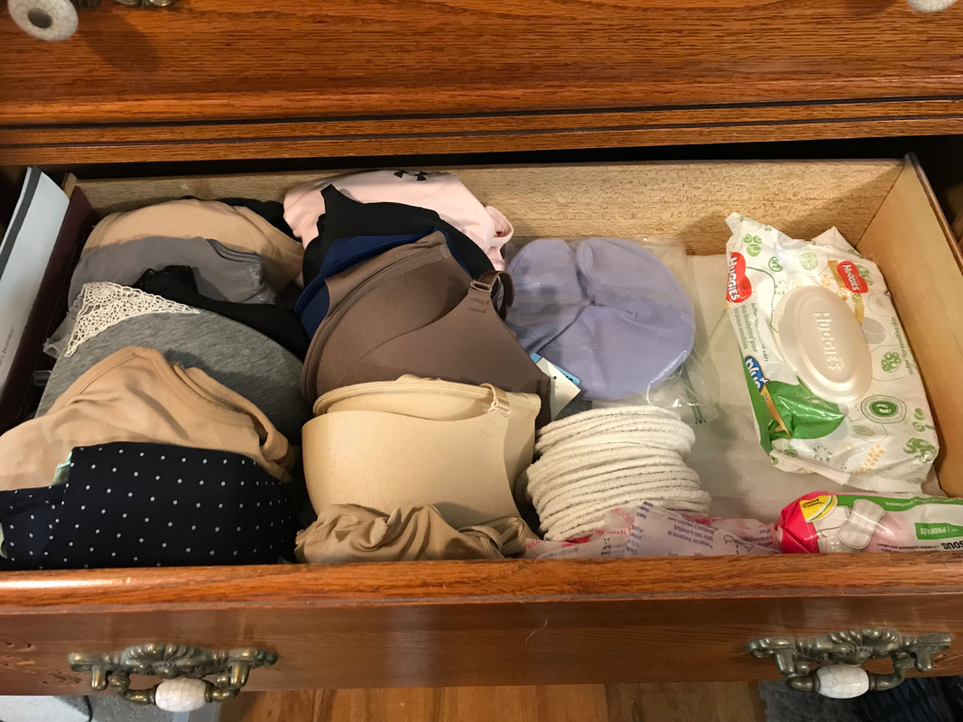 Open draw in wooden dresser with three rows of neatly organized bras, bra pads, and baby wipes.