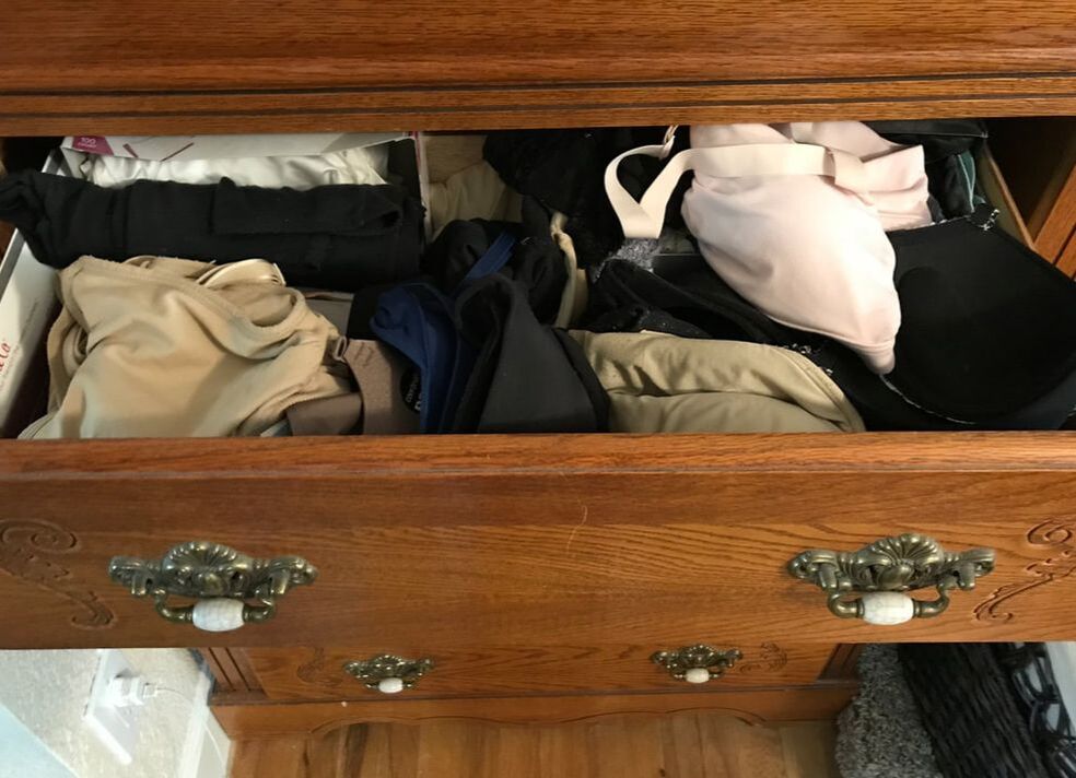 Wooden chest of drawers with one drawer open and showing undergarments stacked haphazardly
